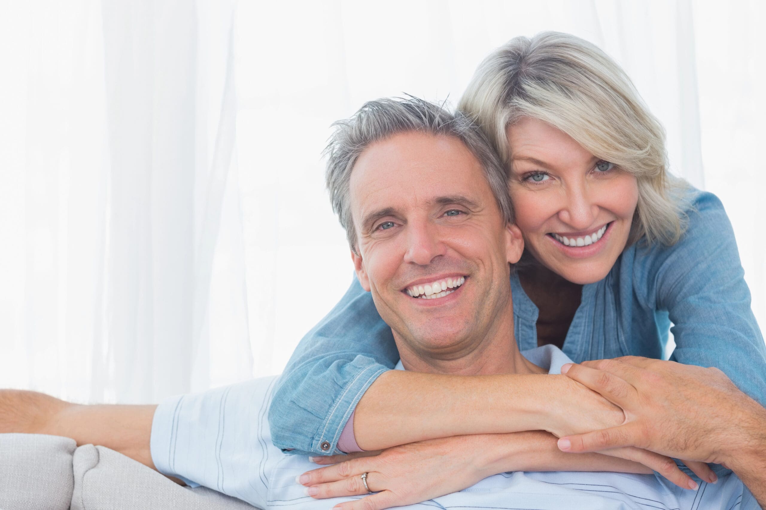 Smiling middle-aged couple with bright teeth, showcasing the confidence and natural look of high-quality dentures. Learn about dentures cost and how they can restore your smile.