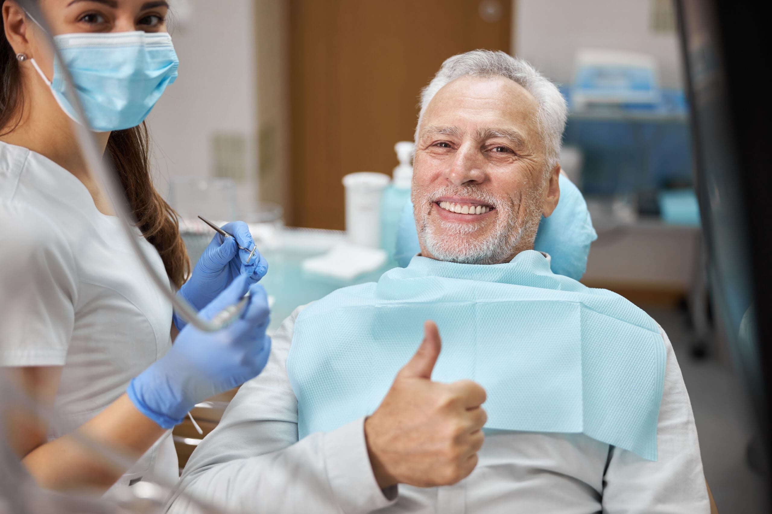 Happy senior man at the dentist's office giving a thumbs-up, showcasing confidence after receiving affordable types of dentures for a natural and comfortable smile.